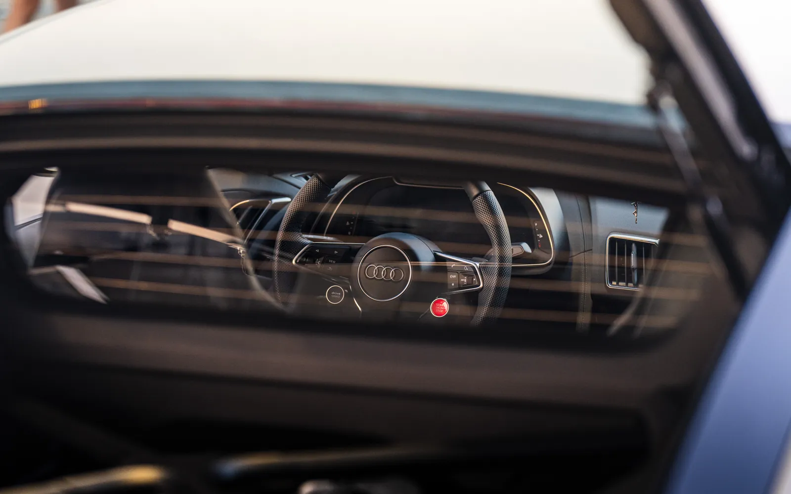 Zoomed into the steering wheel from the back window of a White Audi R8