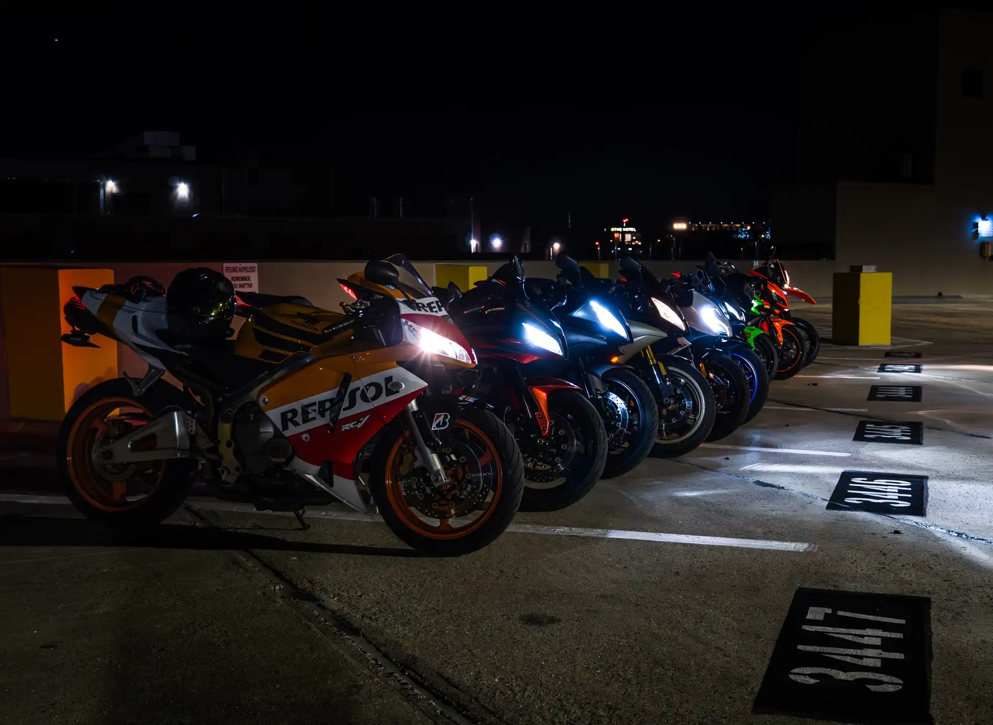 Lineup of Nine colorful Motorcycles with their headlights on at night time on parking garage