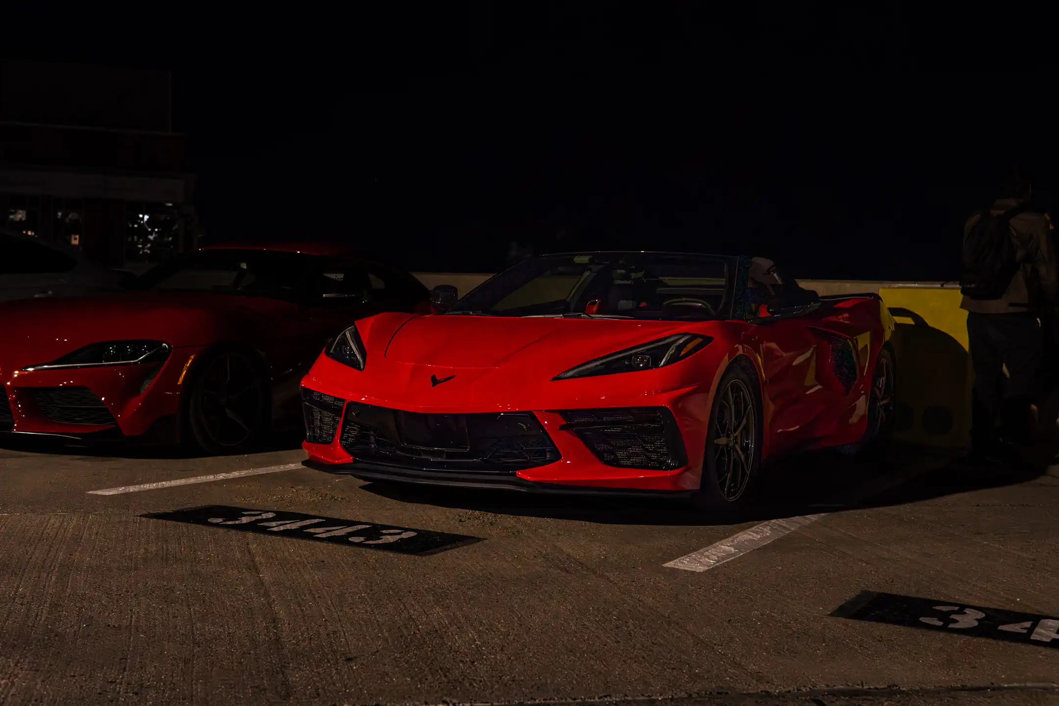 Red Corvette next to Red Supra at night on parking garage in Maryland by Antlophotography